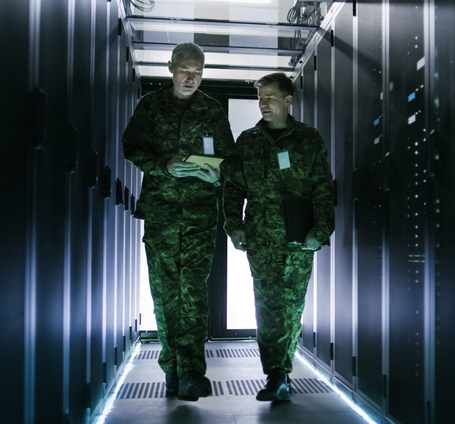 Two Military Men Walking in Data Center Corridor. One Uses Table