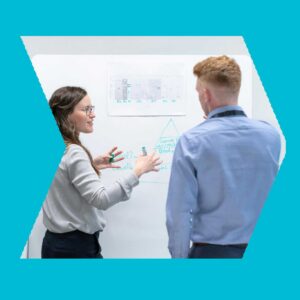 A woman and a man standing in front of a whiteboard discussing the design of OT security services