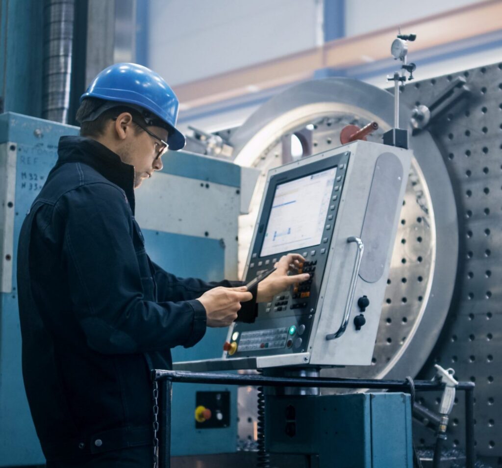 A man in a hard hat stands before a factory computer
