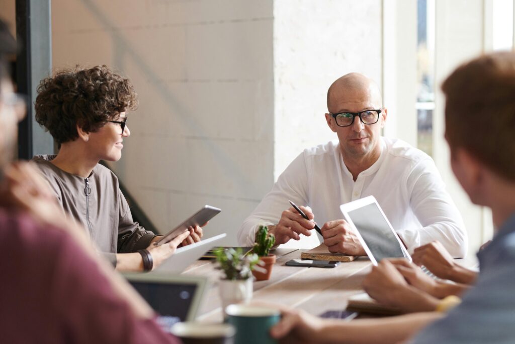 Casually dressed business people sit talking round a meeting table