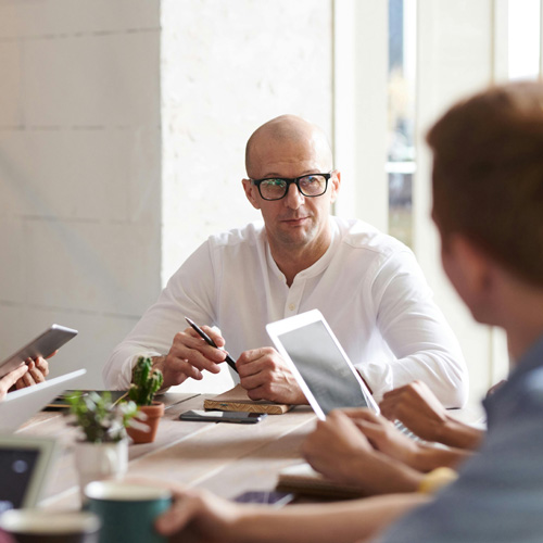 Casually dressed business people sit talking round a meeting table