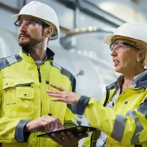 Close up of two men and a woman in hard hats and hi-viz jackets talking in an industrial environment