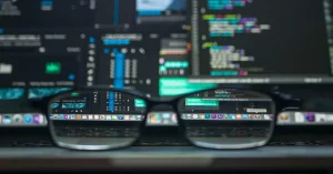 A pair of reading glasses sitting on a desk in front of a computer screen displaying data and code